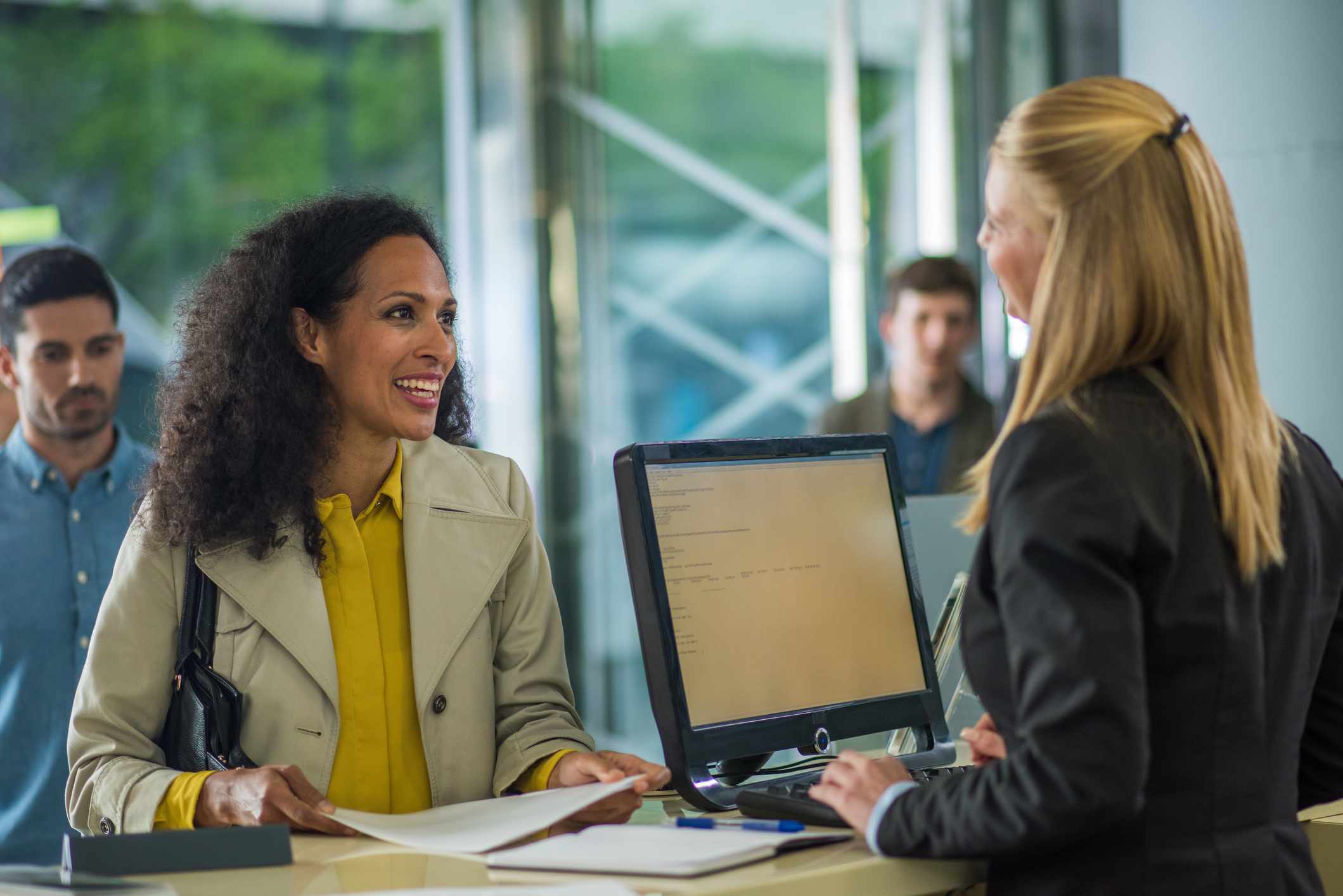 Customer holding document and smiling while bank teller serving.