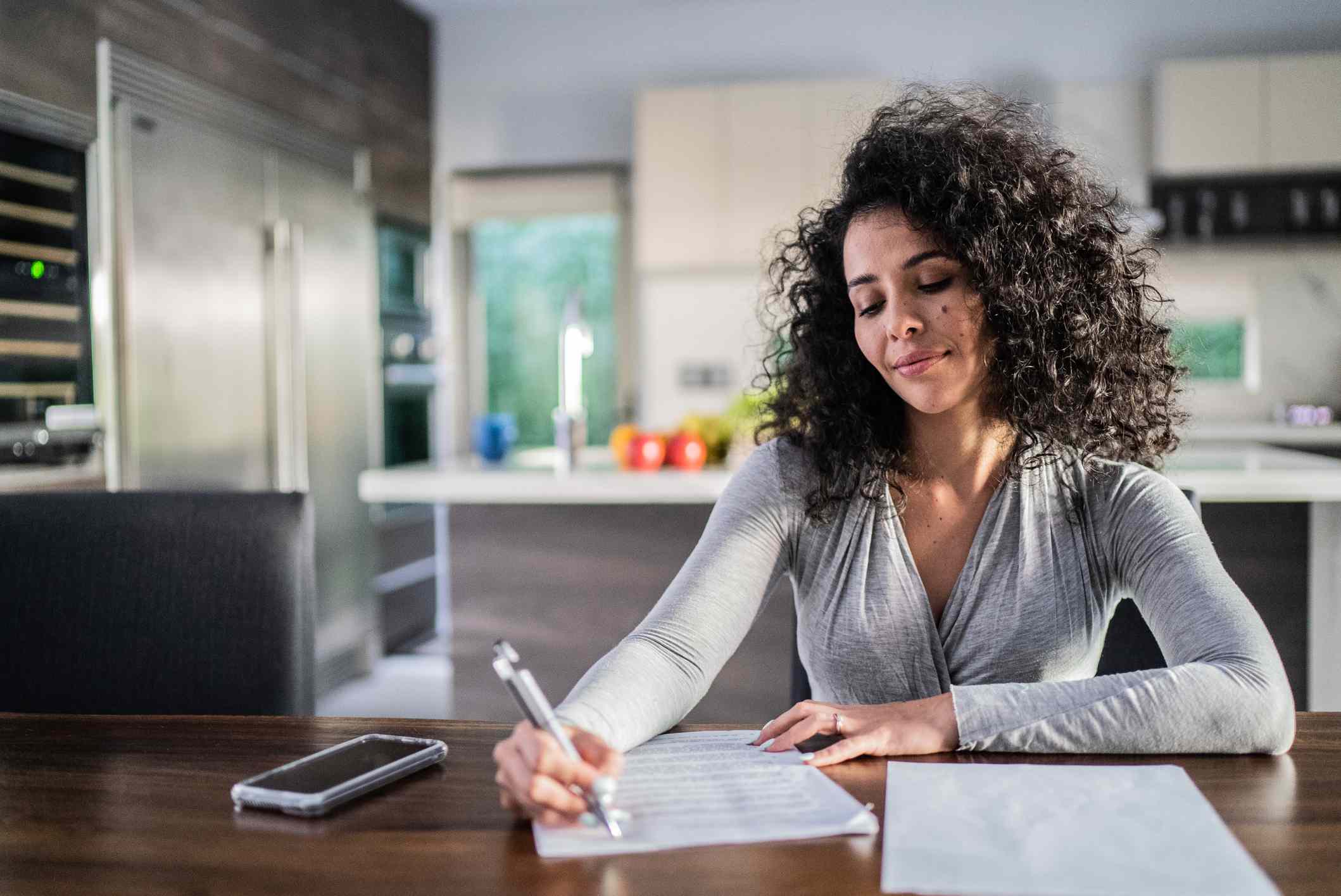 Woman fills in documents at a kitchen table.