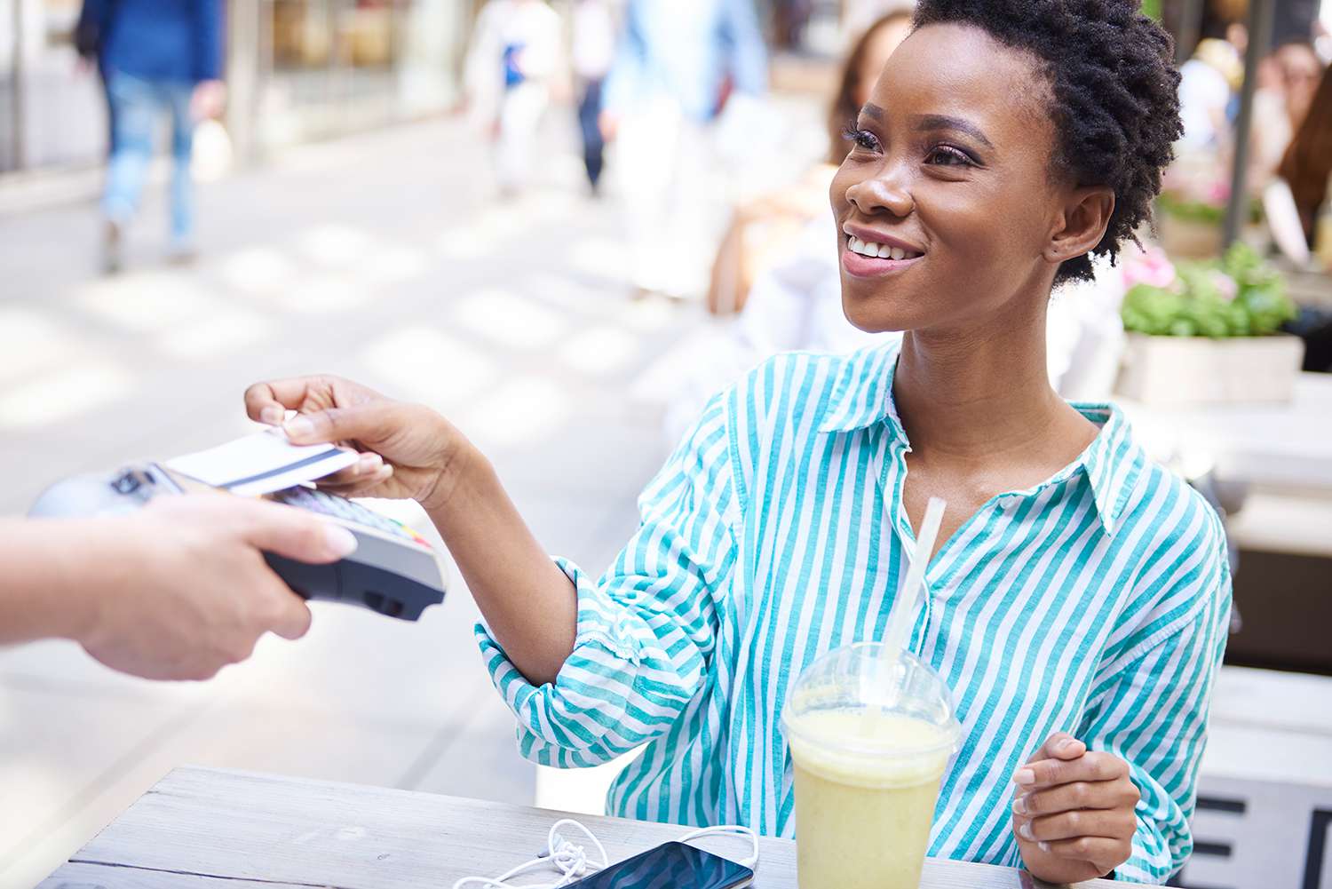 Portrait of smiling woman paying by credit card at pavement cafe.