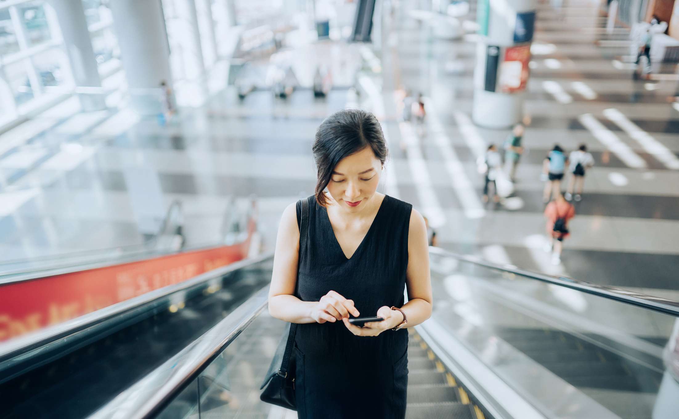 Woman looking at her phone while riding an escalator.