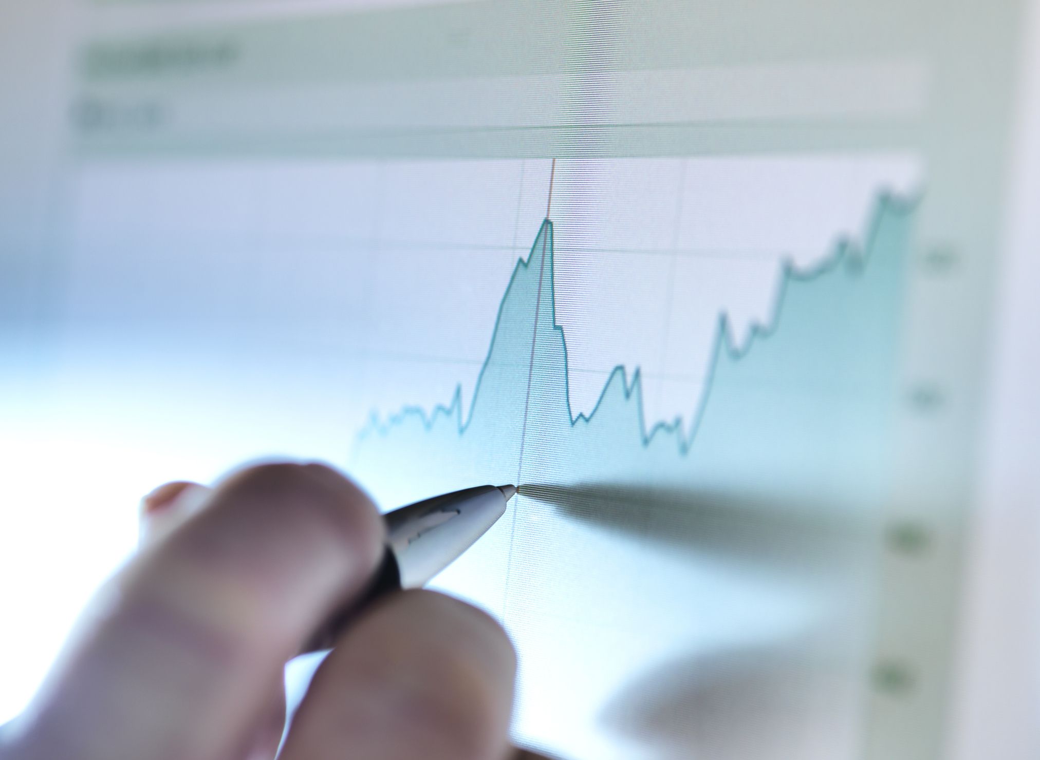 Hand of a stock broker analyzing line graph on computer screen.