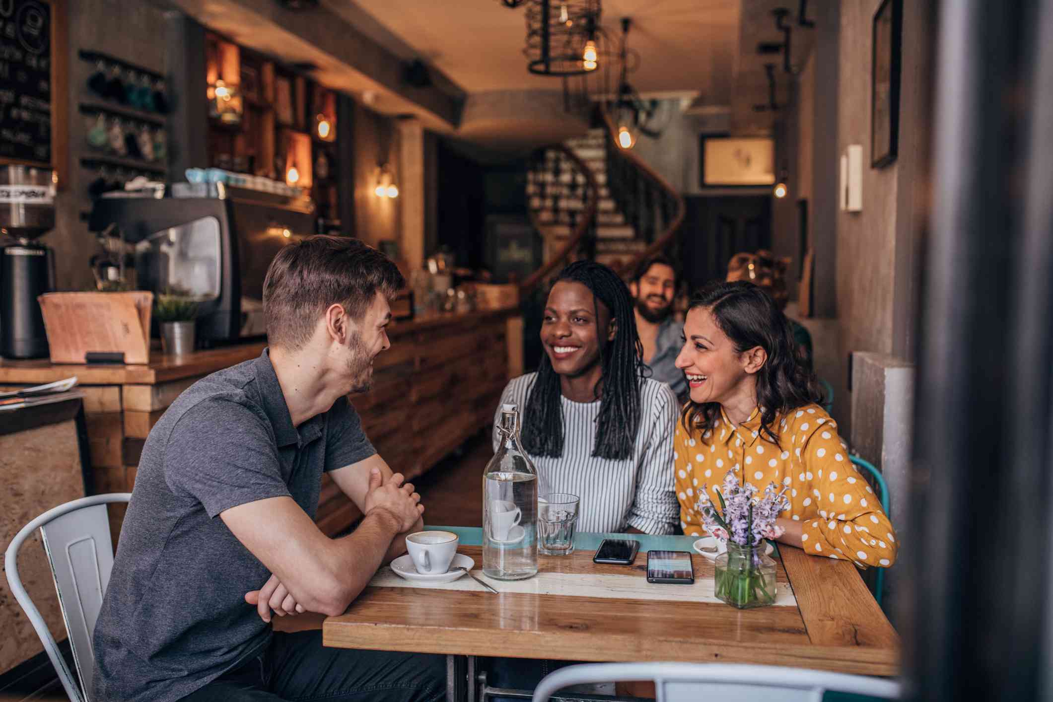 three friends sitting together in a coffee shop talking