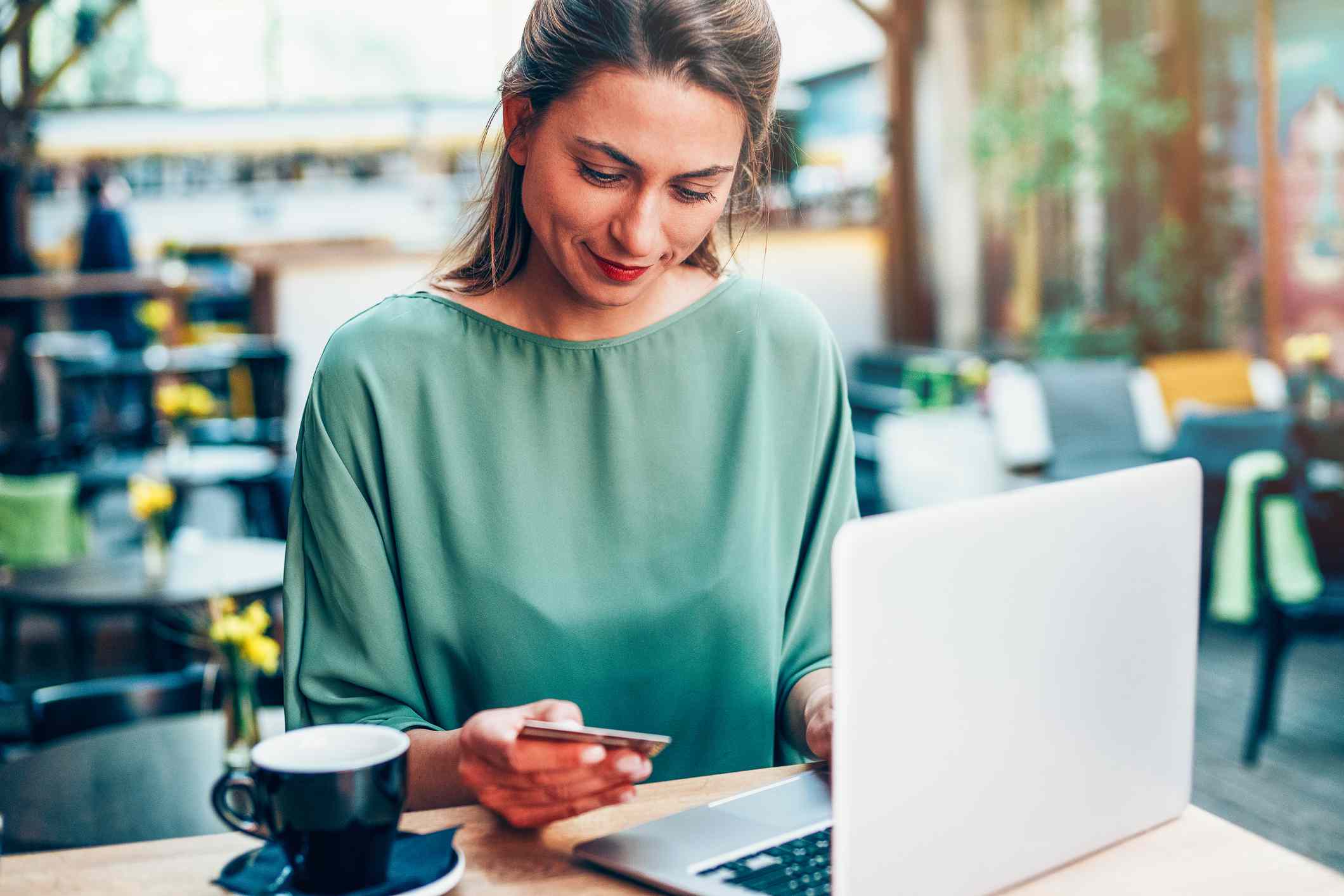 person in green shirt looking at credit card while sitting in coffee shop